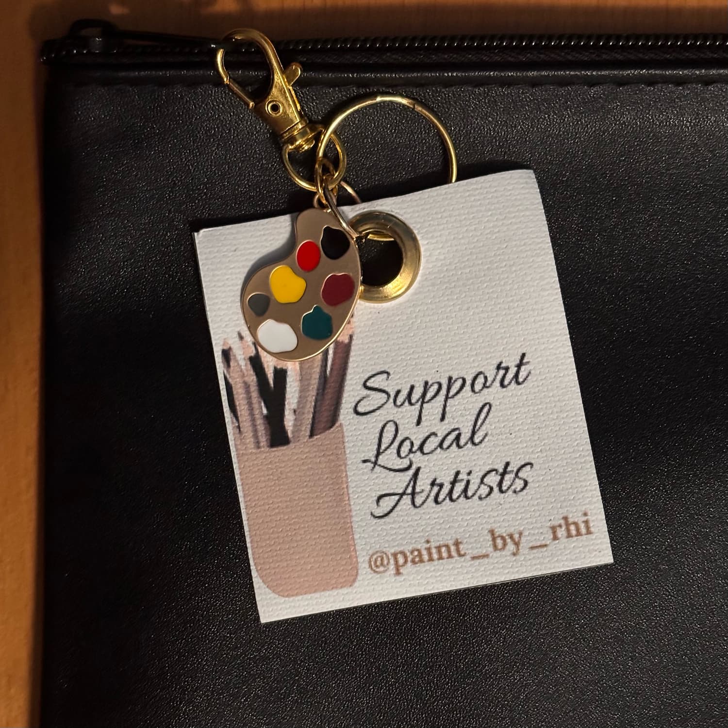 Support Local Artists keychain clipped onto a bag